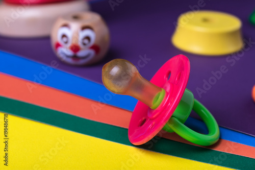 Children's pacifier with a colored wooden pyramid clown on colored paper