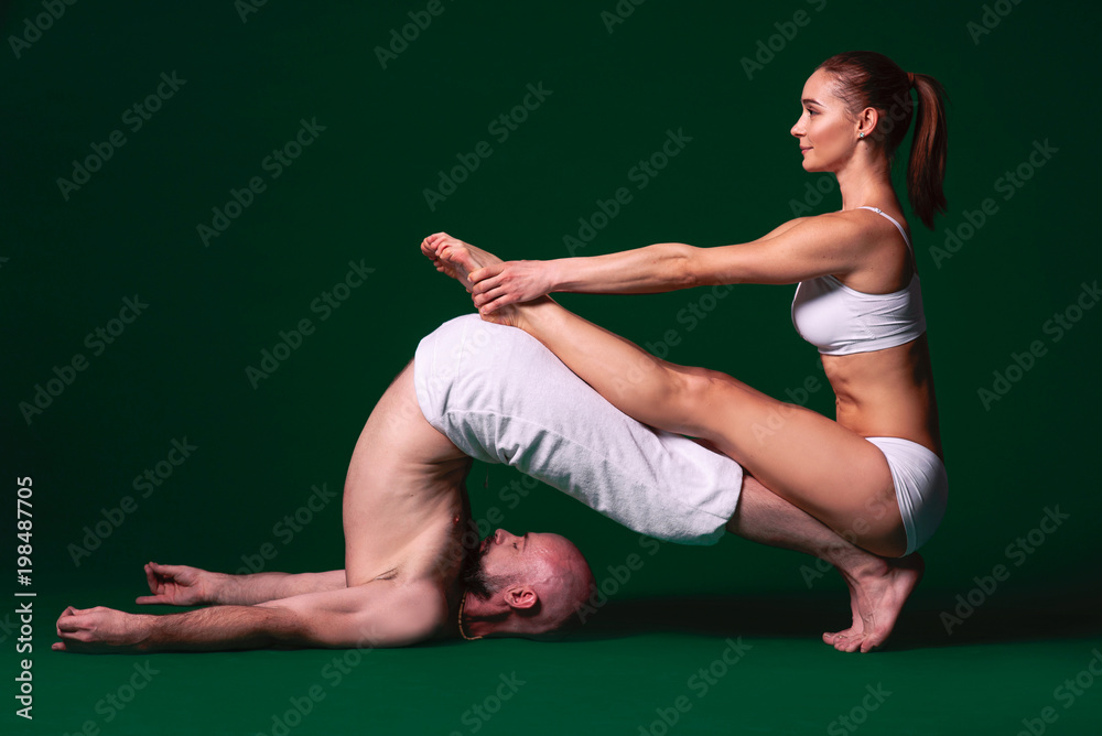 Obraz premium Beautiful sporty woman and man in white clothes doing yoga asanas together indoor on green background