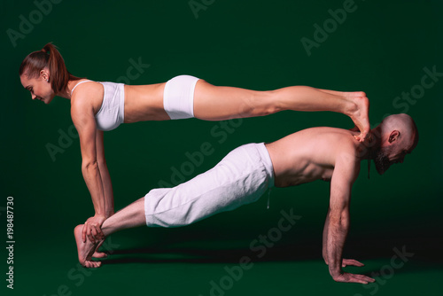 Beautiful sporty woman and man in white clothes doing yoga asanas together indoor on green background