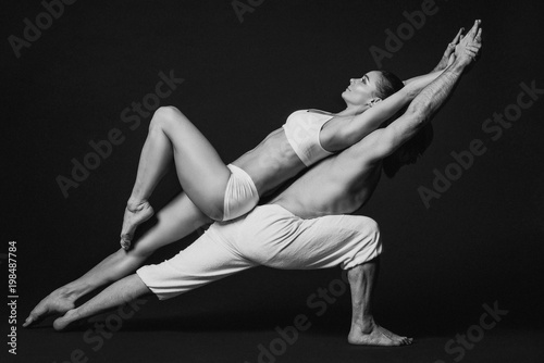 Monochrome portrait of beautiful sporty couple: woman and man in white clothes doing yoga asanas together indoor 