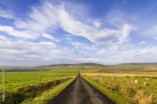 Long straight road with open fields to the sides, Orkney Island, Scotland, United Kingdom.