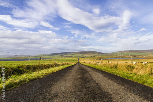 Long straight road with open fields to the sides, Orkney Island, Scotland, United Kingdom.