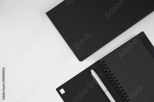 Flat lay image of black book and silver pen over white background