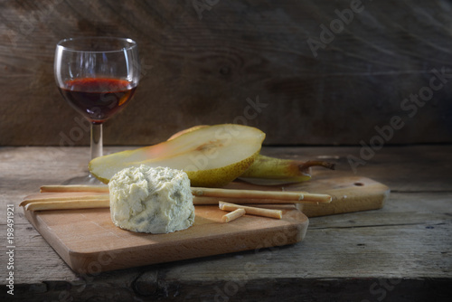 creamy blue stilton cheese, port wine, pear and some nibble sticks on a cutting board against a dark rustic wooden background, copy space