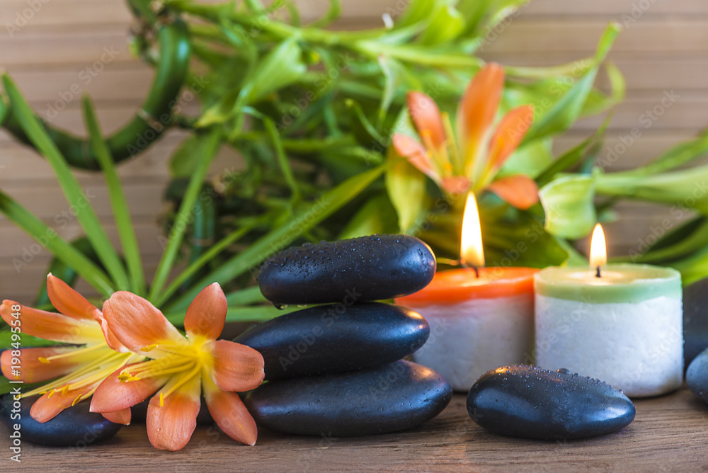Spa concept with massage stones, orange flowers, green bamboo stems and burning candles