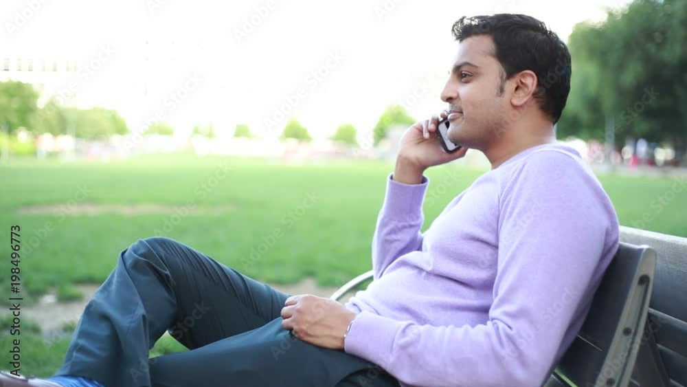 Closeup portrait, handsome young business man, happy guy in purple sweater, using cell phone, smiling, having pleasant conversation, isolated outside background. Human emotions, expression Closeup portrait, handsome young business man, happy guy in purple sweater, using cell phone, smiling, having pleasant conversation, isolated outside background. Human emotions, expression