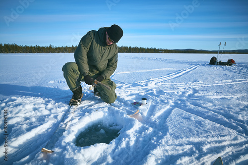 Ice fisherman on winter lake prepares fishing tackle for winter fishing.