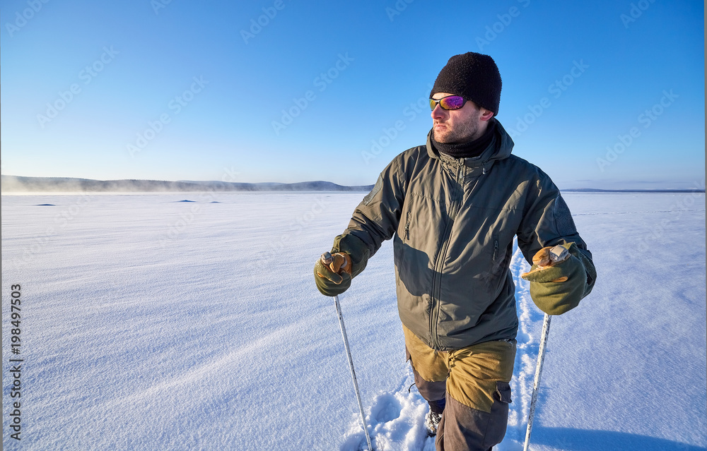 Freedom is in us.  Young man in outdoors clothes is riding on wooden skis on snow on sunny day in the open area.