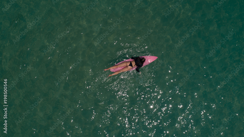 Fototapeta premium Aerial top view of beautiful young woman in swimsuit with pink surfboard enjoying her holiday in amazing clear sea water