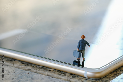 Travel and technology concept. Businessman miniature figure with suitcase standing and walking on smart phone.