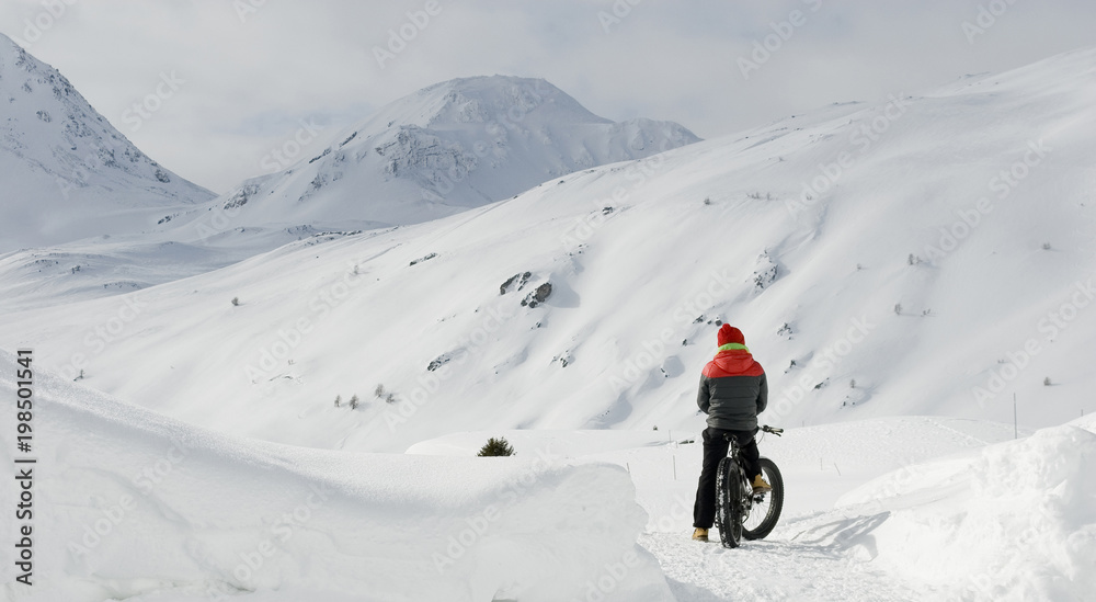 man with electric bicycle, e-bike, ebike, snow road, look mountains and  horizon, bike with wide wheels to go on snow, called fatbike, winter, cold,  alps, freeride, Simplon Pass, Switzerland Stock Photo