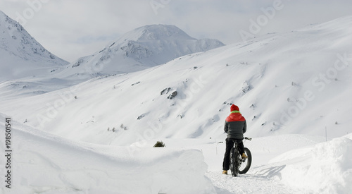man with electric bicycle, e-bike, ebike, snow road, look mountains and horizon, bike with wide wheels to go on snow, called fatbike, winter, cold, alps, freeride, Simplon Pass, Switzerland