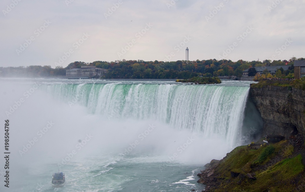 Beautiful and impressive panorama of the Niagara Falls in Ontario (Canada) on a bright colorful (red, orange, yellow) autumn day with water crashing down the falls onto rocks creating lots of mist