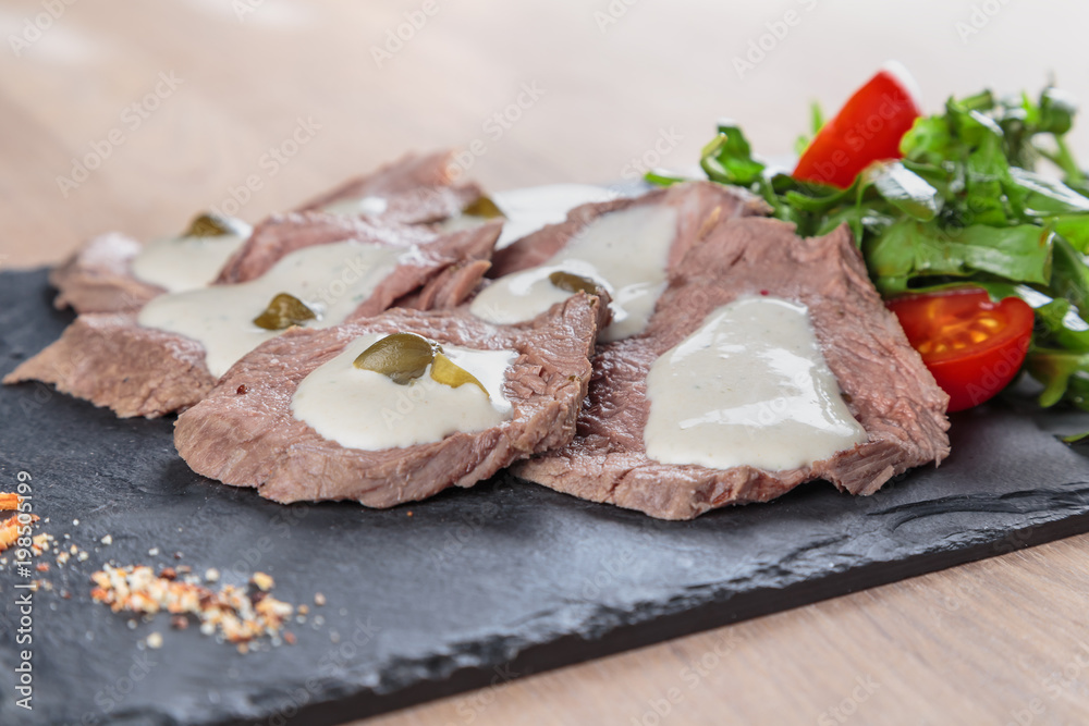 boiled beef tongue with sauce, capers and greens on a black granite tile boiled beef tongue with sauce, capers and greens on a black granite tile