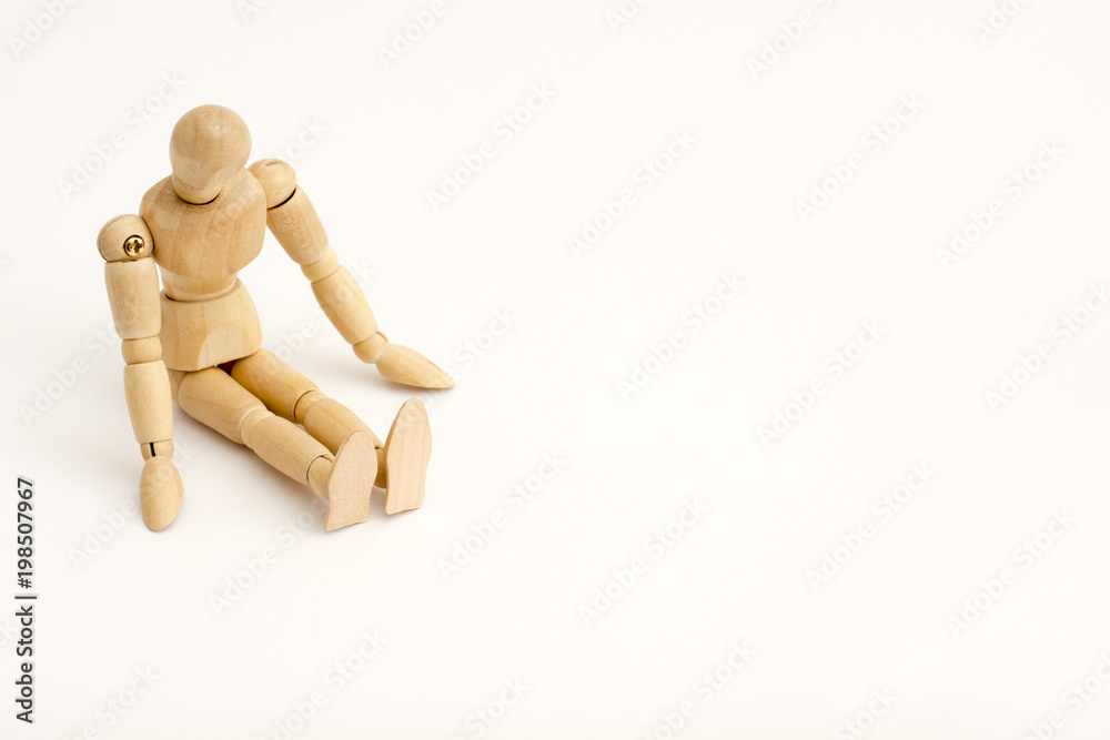 A wooden person sits on the floor, in the corner, his head slightly turned right und down, he turned to the viewer A wooden person sits on the floor, in the corner, his head slightly turned right und down, he turned to the viewer