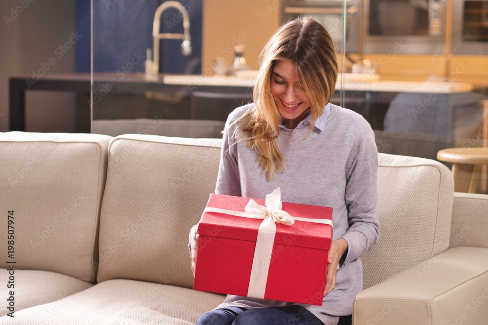 A girl at home opens a gift bag that has arrived. The package can be a gift or an order arrived thanks to online shopping. Concept of: shopping, love, gift, anniversary.