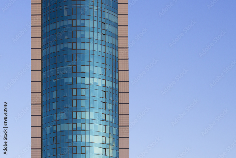 Obraz premium A multi-storey brick building under construction, against a blue sky background. High multi-story building. Skyscraper. Blue windows. Mirror