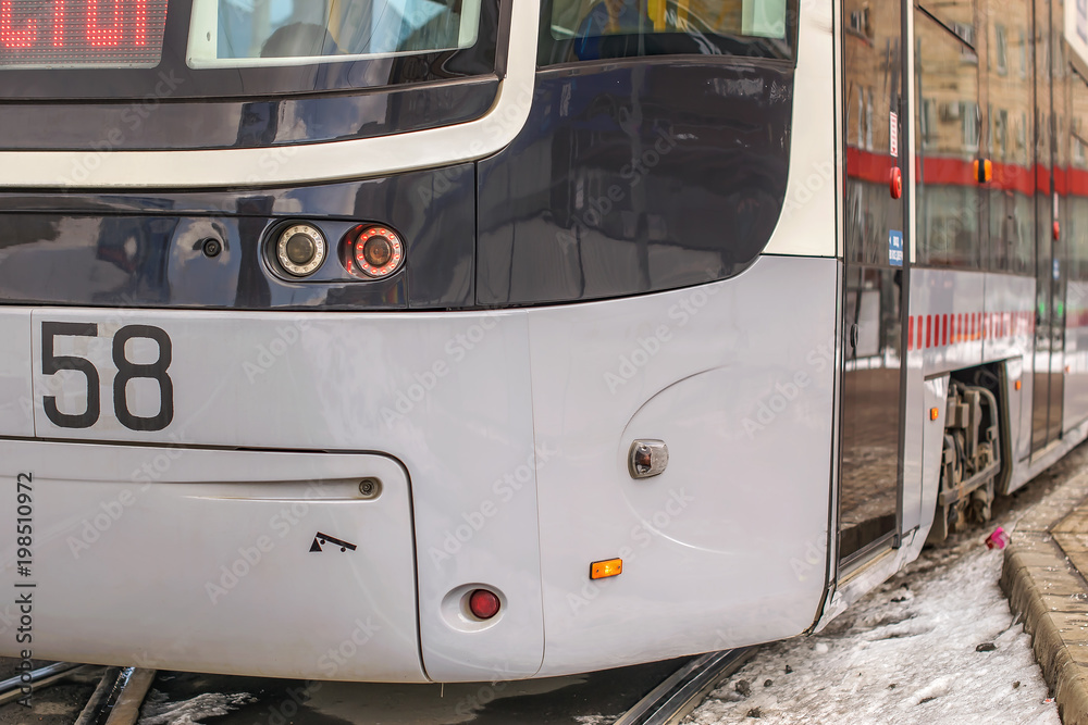 front of the modern tram urban environmental electric transport with headlights on the rails near the stop in the winter city with snow