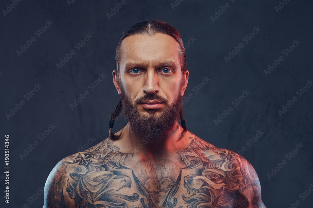 Fototapeta premium Close-up portrait of a muscular bearded tattoed male with a stylish haircut, isolated on a dark background.