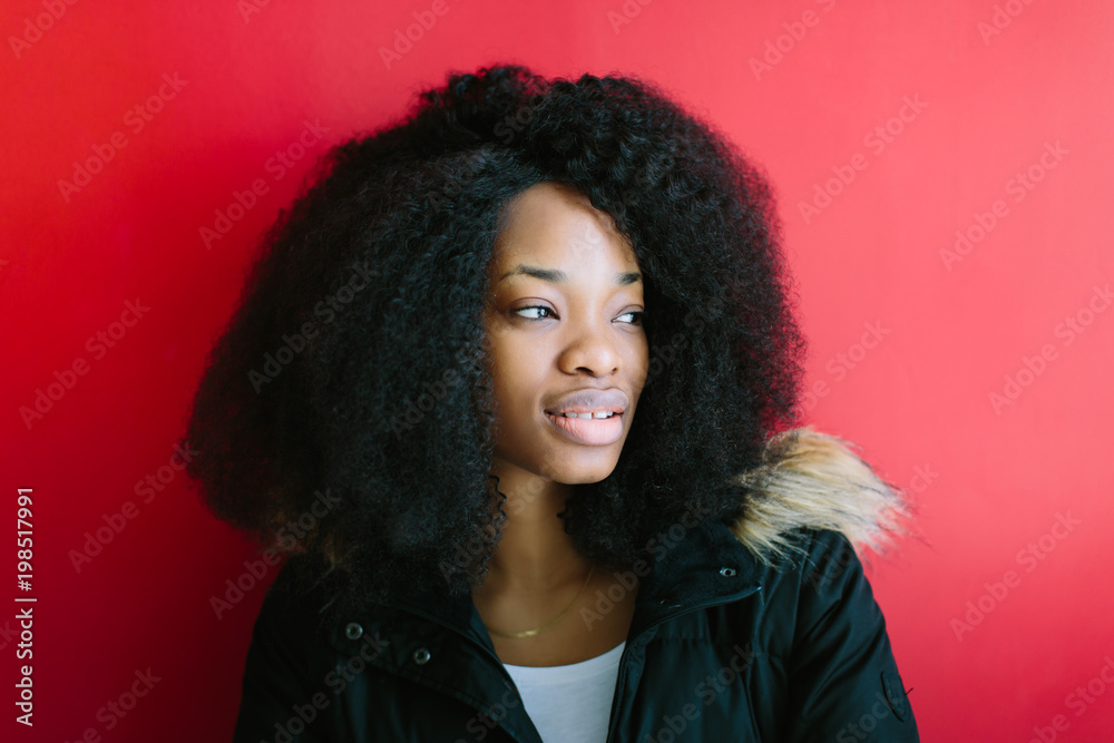 Young beautiful African American girl in a black coat smiling on red background Young beautiful African American girl in a black coat smiling on red background