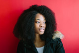 Young beautiful African American girl in a black coat smiling on red background