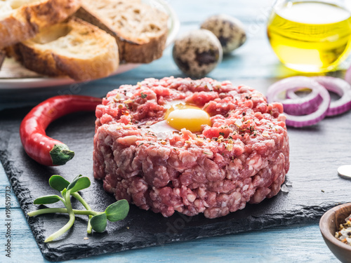 Steak tartare served with raw quail egg yolk, chilly pepper and bread. Meat dish.
