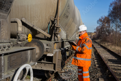 A railway maintenance Inspector wearing high visibility clothing and protective safety work wear examining a tanker wagon at the track side