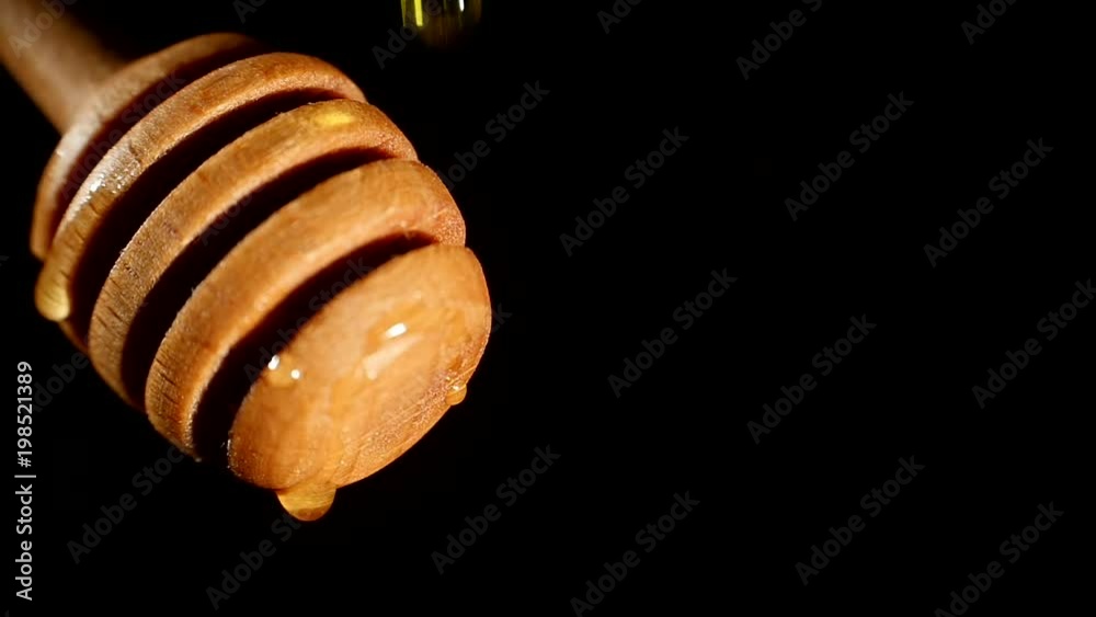 Thick honey dripping from the honey spoon, one drop, on black background, close up
