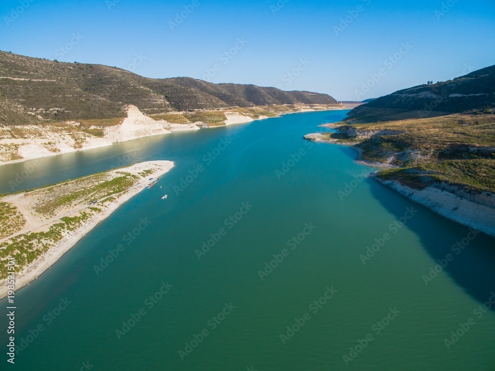 Aerial Bird's eye view of artificial lake at the largest dam in Cyprus, Kouris reservoir, Limassol. View of the river split peninsula, earthfill embankment and hills around water from above.