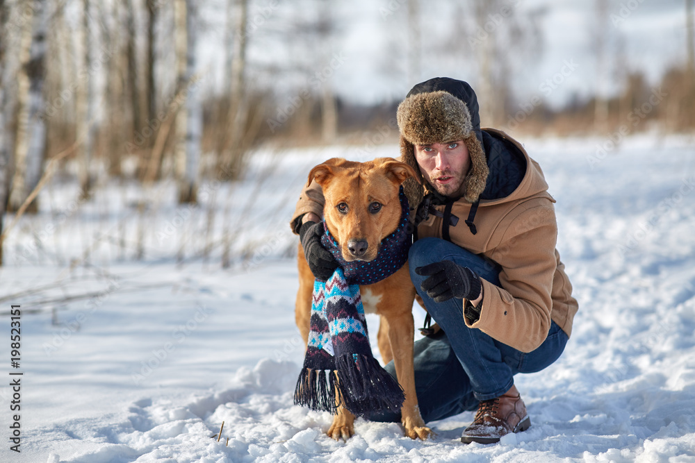 Golden retriever in winter clothes with a scarf and fur hat. a man's friend is sitting next to the landlord