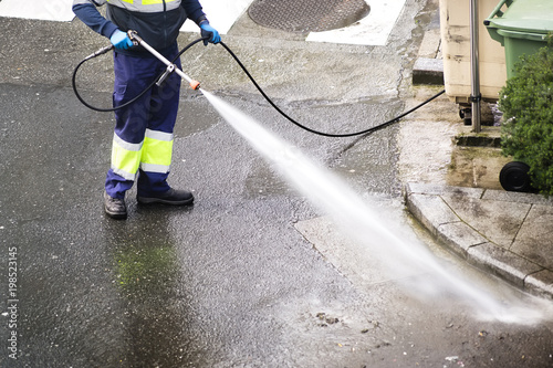 sweeper gardener  cleaning  the city street with pressure water photo