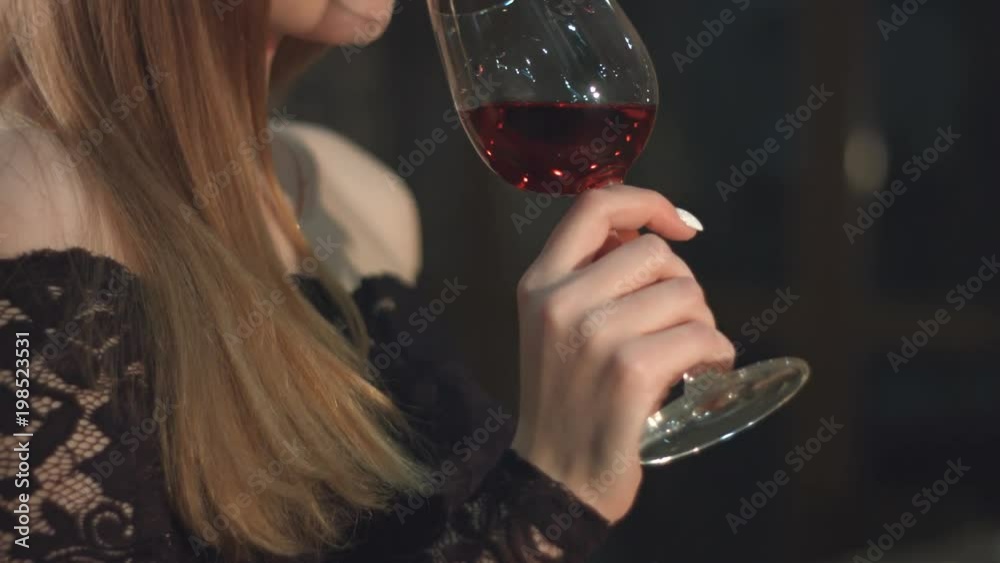 A pretty girl tasting red wine in a wine cellar.
Slow motion. Close-up. Vertical pan.
A glass of wine in her hand. The face of the girl in profile. She takes a sip and looks up.