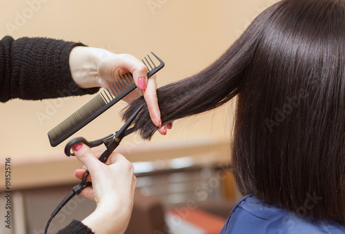 The hairdresser does a haircut with hot scissors of hair to a young girl, a brunette in a beauty salon.