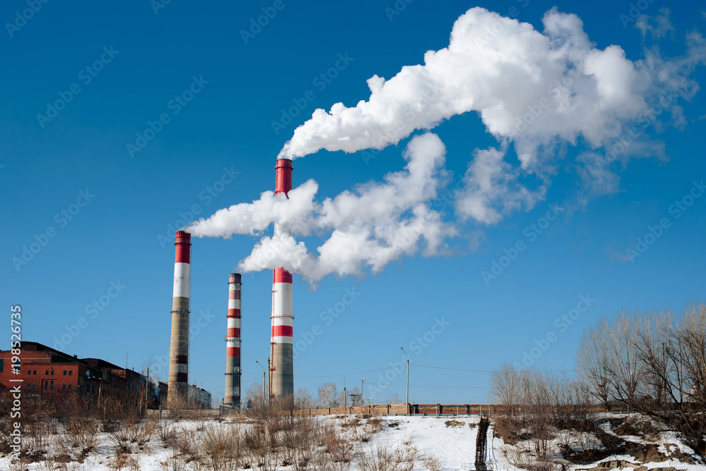 factory pipes with white smoke near the river in winter factory pipes with white smoke near the river in winter