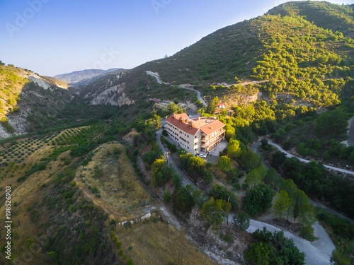 Aerial bird's eye view of christian greek orthodox Holy Monastery of Panayia Amasgous in Monagri village,Limassol,Cyprus. The traditional stone ceramic roof tiled church in the forest slope from above photo