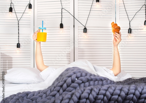 A woman is having breakfast in bed. Orange juice and a croissant.
