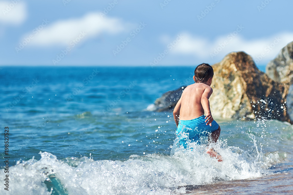 Cute Caucasian boy is running in the water along the sea shore. Cute Caucasian boy is running in the water along the sea shore.