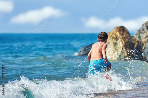 Cute Caucasian boy is running in the water along the sea shore.