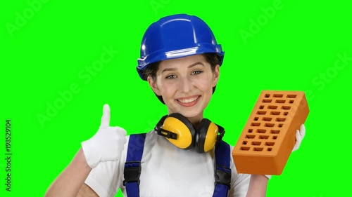 Girl builder i carries a brick for construction and show thrumbs up. Green screen photo