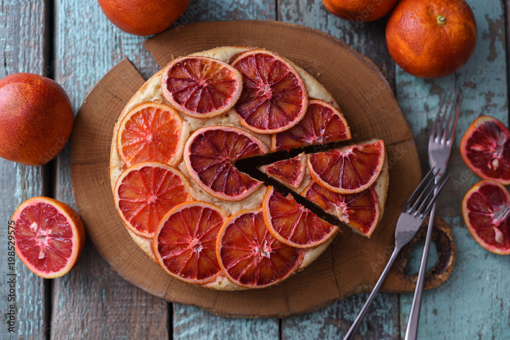 Homemade fruit cake. Round blood orange cake cut on oak board on shabby blue background Homemade fruit cake. Round blood orange cake cut on oak board on shabby blue background