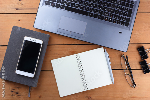 Laptop on a wooden background, a job on an old table, smartphone and notebook, pen and glasses in the workplace, copy space, office space in a minimalist style, art