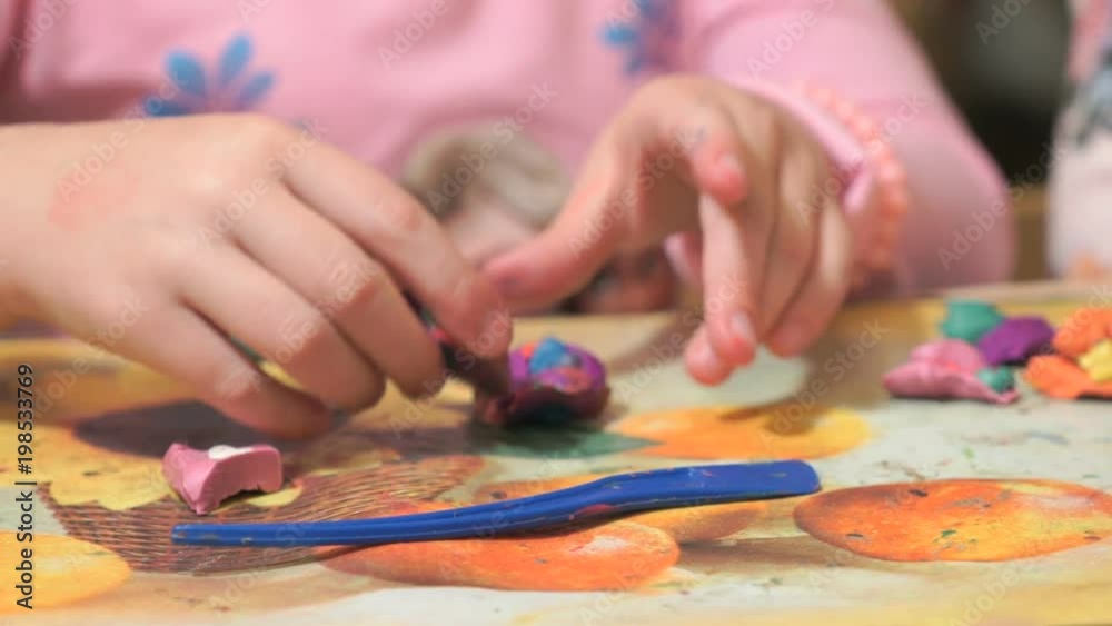 Unknown little child sitting at the desk sculpts a different figures from made of colored modeling plasticine in the nursery. Development of the art of modeling in children Unknown little child sitting at the desk sculpts a different figures from made of colored modeling plasticine in the nursery. Development of the art of modeling in children