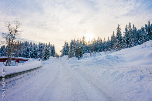 Outdoor view of winter road covered with heavy snow and ice in the forest and a gorgeous sunset view