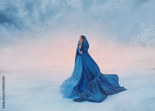 The Snow Queen in a blue raincoat that flutters in the wind. A traveler on a background of sunrise or sunset, and a frozen valley covered with snow and clouds, a place where heaven meets the earth.