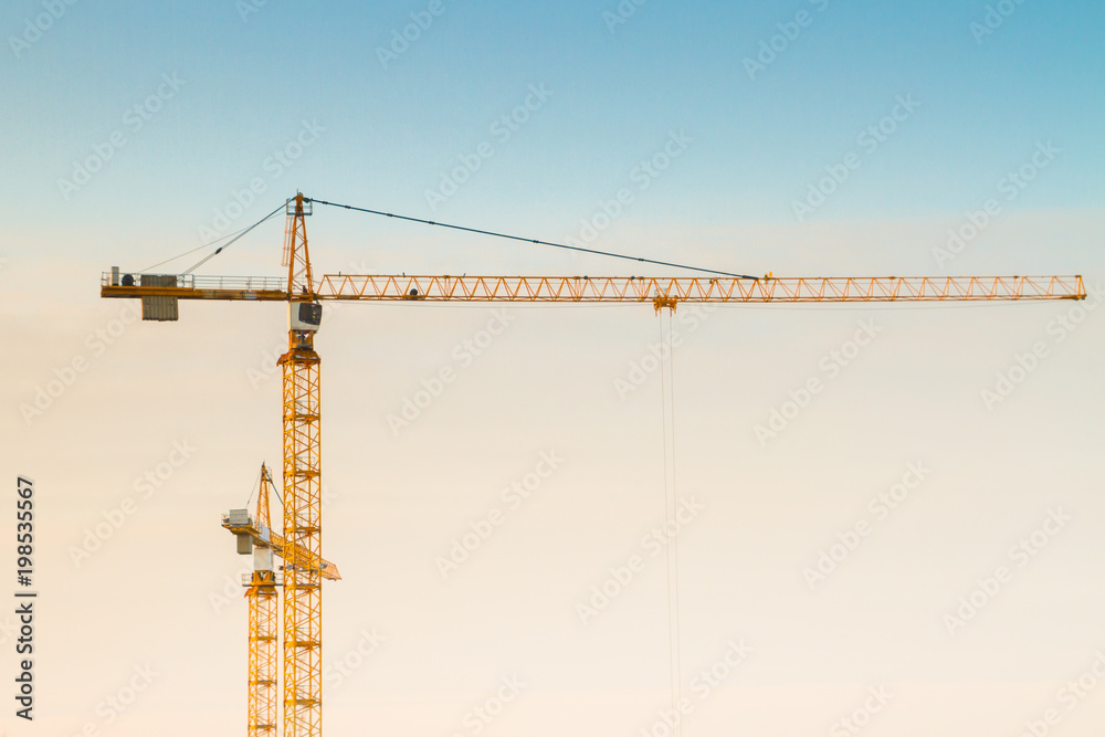 Construction cranes at a construction site at sunset in early spring Construction cranes at a construction site at sunset in early spring