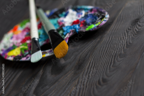 Brushes and art palette with paint on brown wooden background photo