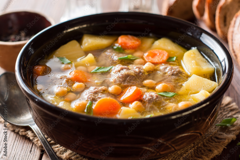 Soup with meatballs, vegetables and chickpea on wooden table