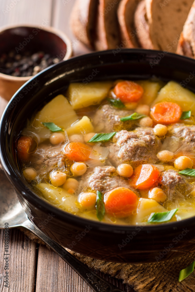 Soup with meatballs, vegetables and chickpea on wooden table Soup with meatballs, vegetables and chickpea on wooden table
