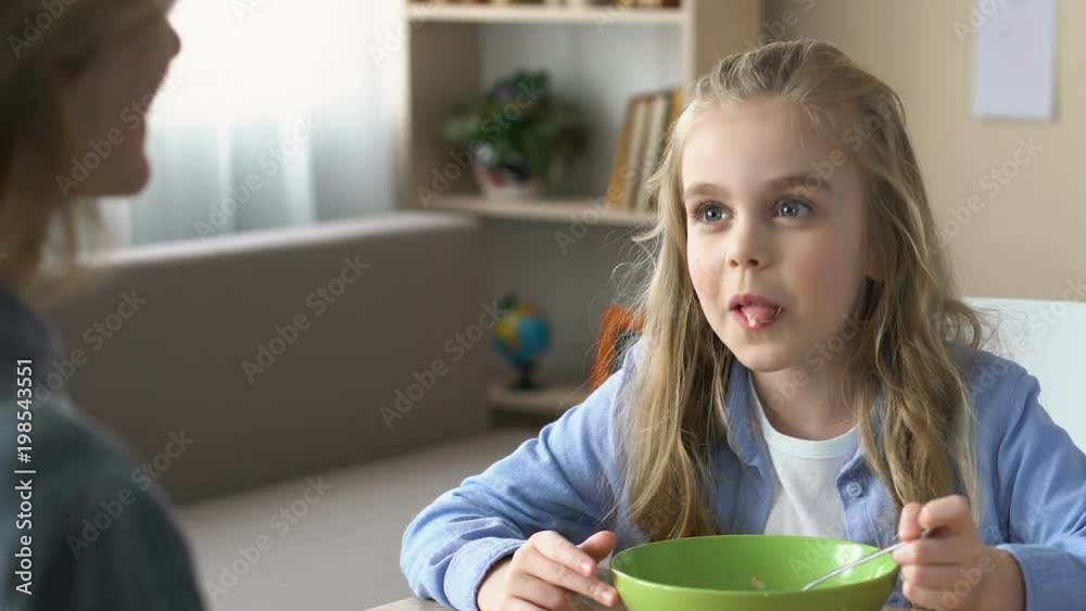 School girl eating breakfast with mother sitting front, spending time together School girl eating breakfast with mother sitting front, spending time together