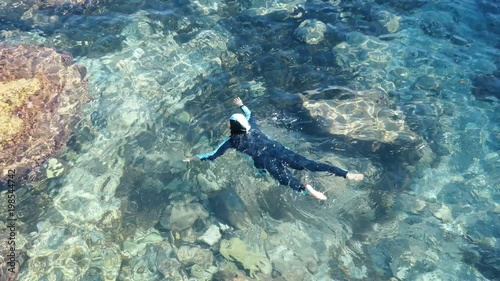 A Muslim woman is swimming in a turquoise sea. Europe.